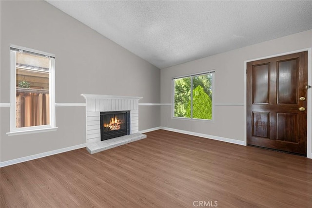 unfurnished living room with hardwood / wood-style flooring, a textured ceiling, lofted ceiling, and a fireplace