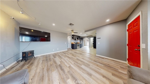 unfurnished living room with ceiling fan, light hardwood / wood-style floors, a wood stove, and a textured ceiling