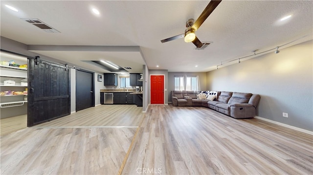 unfurnished living room with light wood-type flooring, a textured ceiling, ceiling fan, a barn door, and track lighting