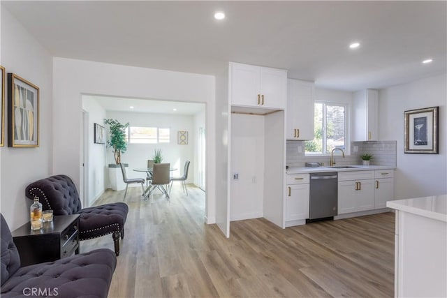 kitchen featuring dishwasher, backsplash, white cabinets, sink, and light hardwood / wood-style flooring