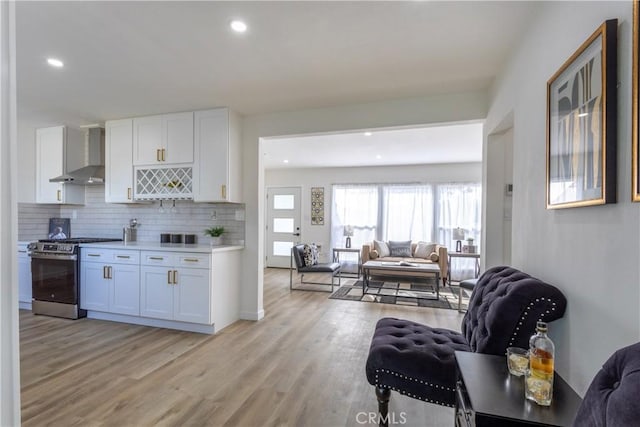 kitchen with wall chimney exhaust hood, white cabinets, light hardwood / wood-style flooring, and stainless steel stove