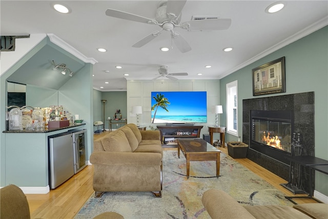 living room featuring a tile fireplace, light hardwood / wood-style floors, ceiling fan, and crown molding