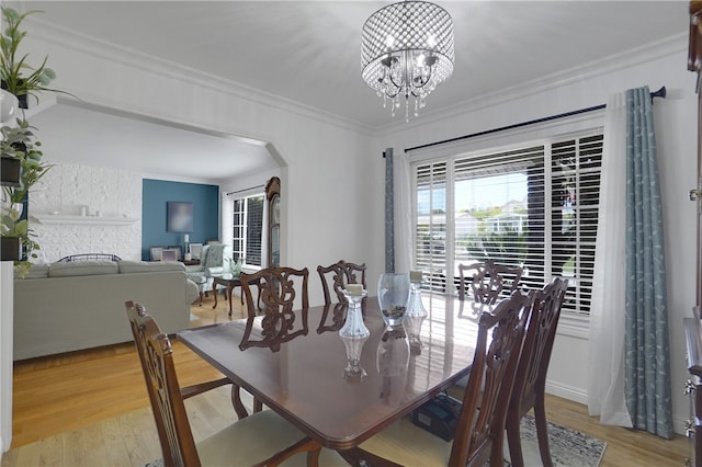 dining area featuring light wood-type flooring, an inviting chandelier, a stone fireplace, and crown molding