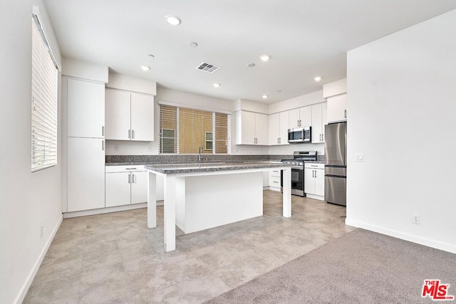 kitchen with white cabinets, appliances with stainless steel finishes, a kitchen island, light colored carpet, and a breakfast bar area