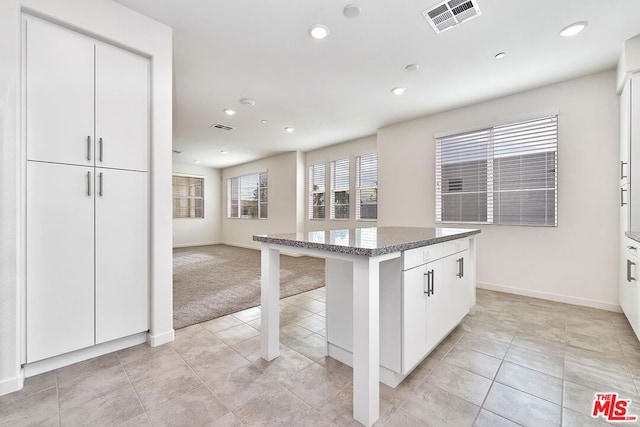 kitchen with white cabinets, a kitchen breakfast bar, a center island, and light colored carpet