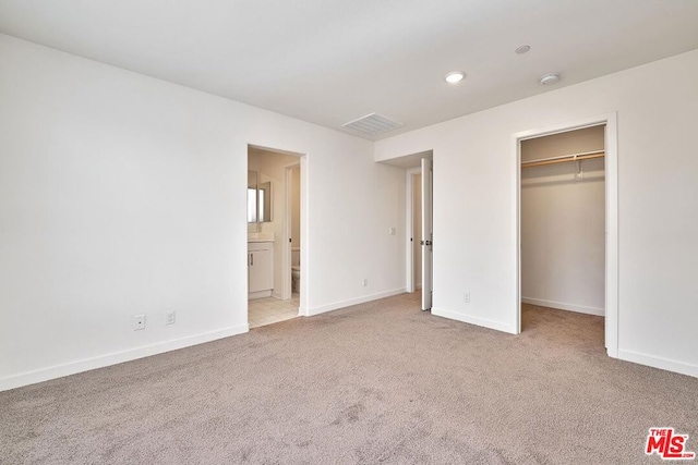 unfurnished bedroom with light carpet, ensuite bathroom, a spacious closet, and a closet