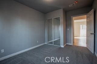 unfurnished bedroom with dark colored carpet and a closet