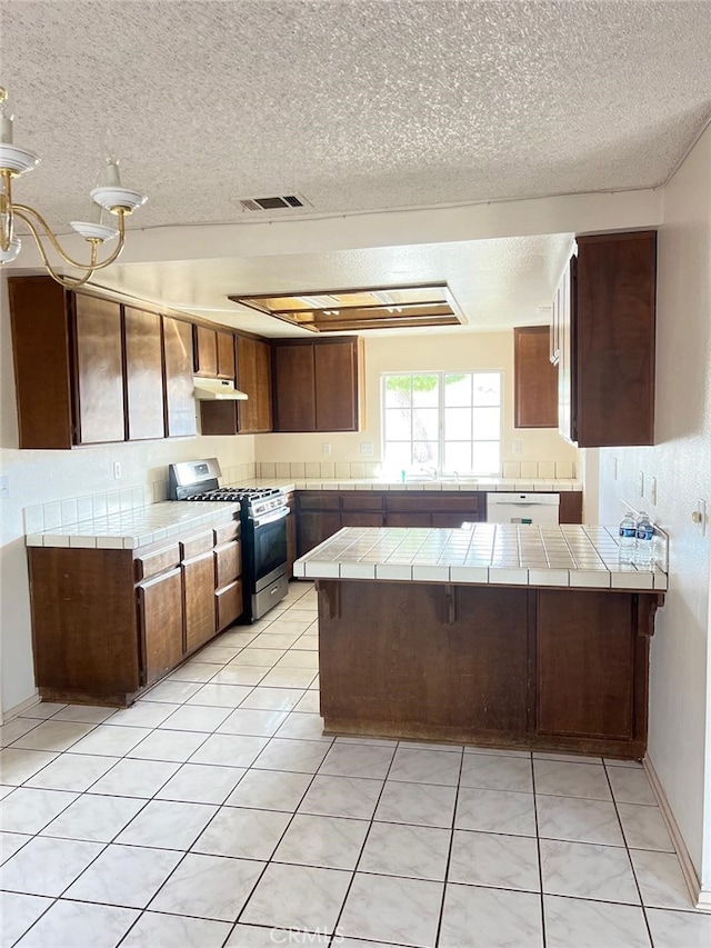 kitchen with light tile patterned flooring, tile countertops, kitchen peninsula, and stainless steel gas range oven