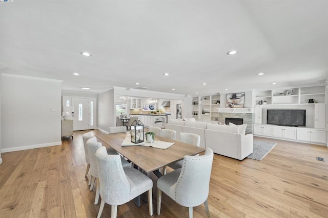 dining area with built in features, light hardwood / wood-style flooring, crown molding, and a stone fireplace