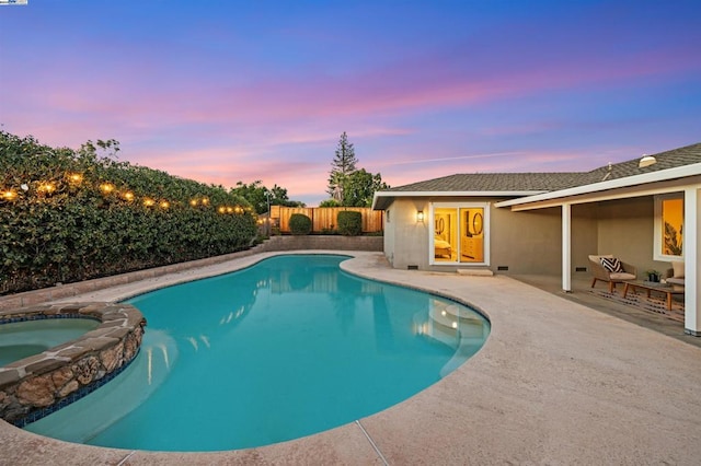 pool at dusk featuring a patio and an in ground hot tub