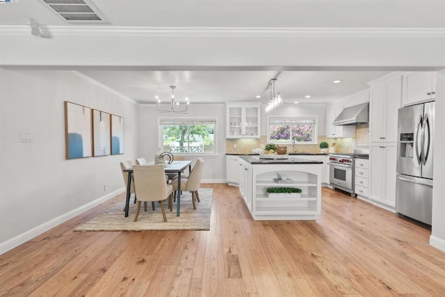 kitchen with decorative light fixtures, white cabinets, wall chimney range hood, and appliances with stainless steel finishes