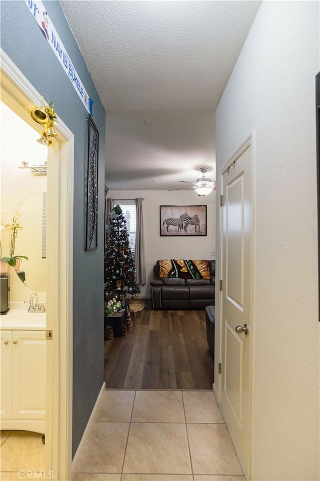 hallway featuring sink, a textured ceiling, and light tile patterned floors