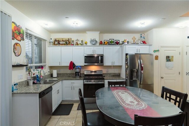 kitchen with light tile patterned floors, white cabinetry, stainless steel appliances, stone counters, and sink