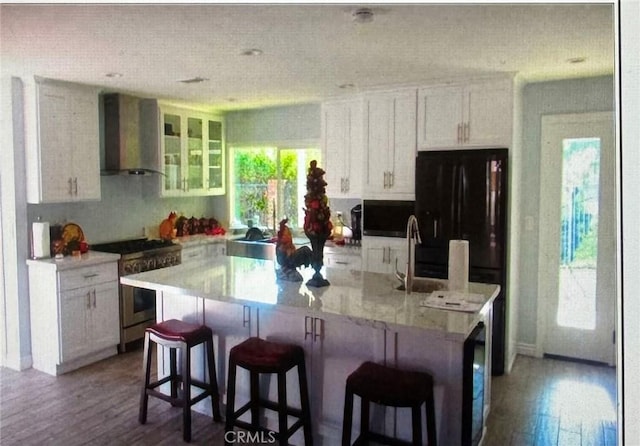 kitchen with white cabinets, gas stove, wall chimney range hood, an island with sink, and plenty of natural light