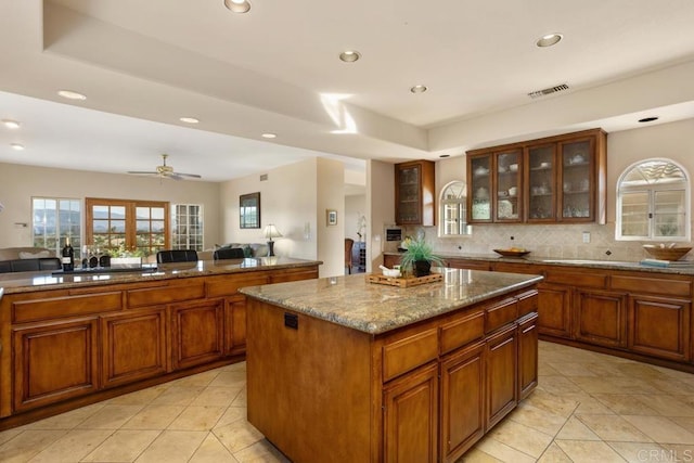 kitchen featuring ceiling fan, backsplash, a center island, sink, and light stone countertops