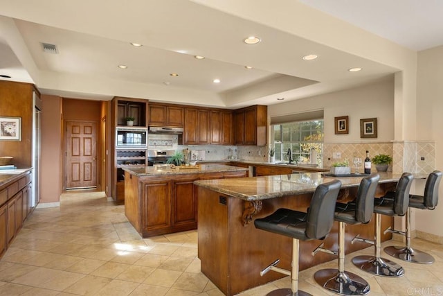 kitchen with light tile patterned floors, stainless steel microwave, dark stone counters, a breakfast bar, and a center island