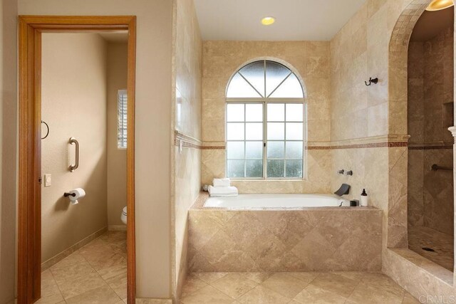 bathroom with toilet, tile walls, and a relaxing tiled tub