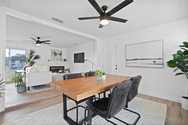 dining room with ceiling fan, light hardwood / wood-style floors, and a brick fireplace