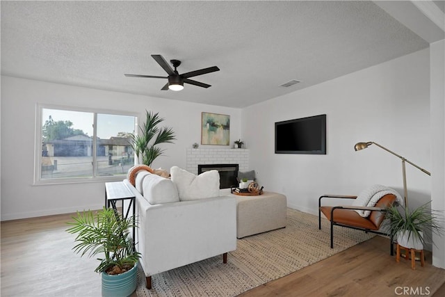 living room featuring ceiling fan, a fireplace, light hardwood / wood-style floors, and a textured ceiling