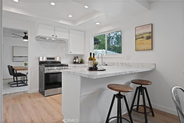 kitchen with kitchen peninsula, gas range, a breakfast bar, and white cabinets