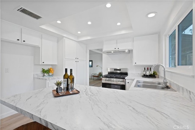 kitchen with white cabinets, stainless steel gas stove, kitchen peninsula, and sink