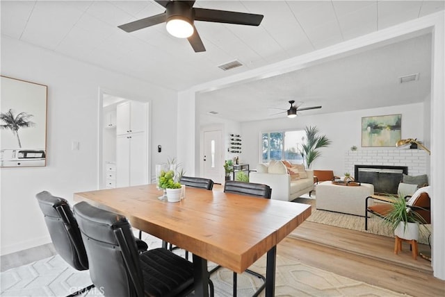 dining area featuring light hardwood / wood-style floors, a brick fireplace, and ceiling fan