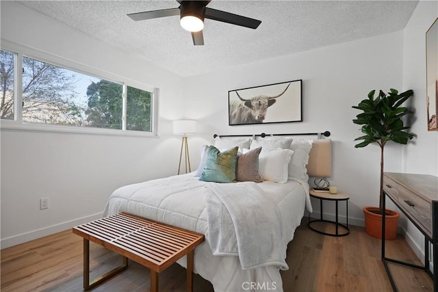 bedroom with ceiling fan, wood-type flooring, and a textured ceiling