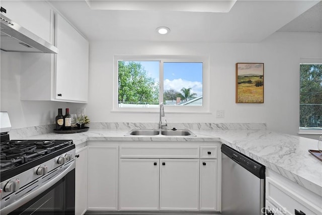 kitchen with sink, wall chimney exhaust hood, a healthy amount of sunlight, white cabinets, and appliances with stainless steel finishes