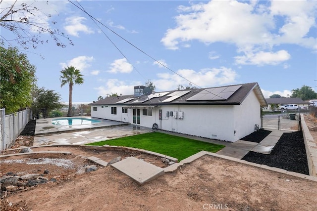 rear view of property with a lawn, solar panels, a patio area, and a fenced in pool