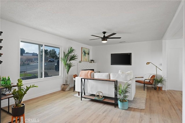 living room featuring a fireplace, a textured ceiling, light hardwood / wood-style flooring, and ceiling fan