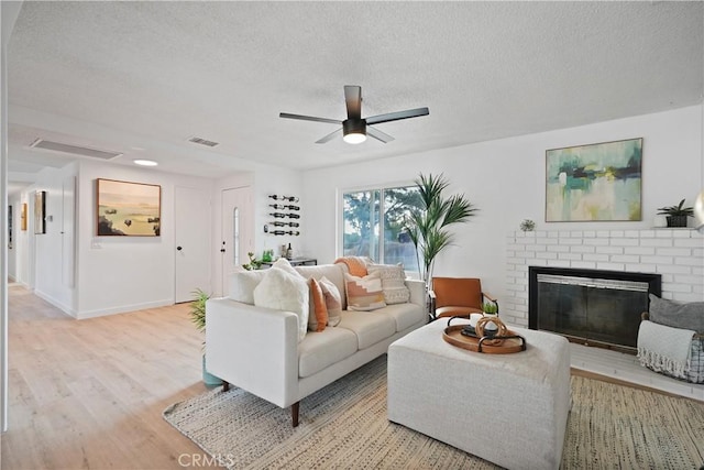 living room with ceiling fan, light hardwood / wood-style flooring, a textured ceiling, and a brick fireplace