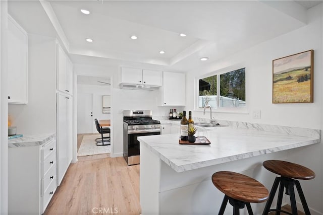 kitchen with a kitchen breakfast bar, stainless steel gas range, sink, light hardwood / wood-style flooring, and white cabinetry