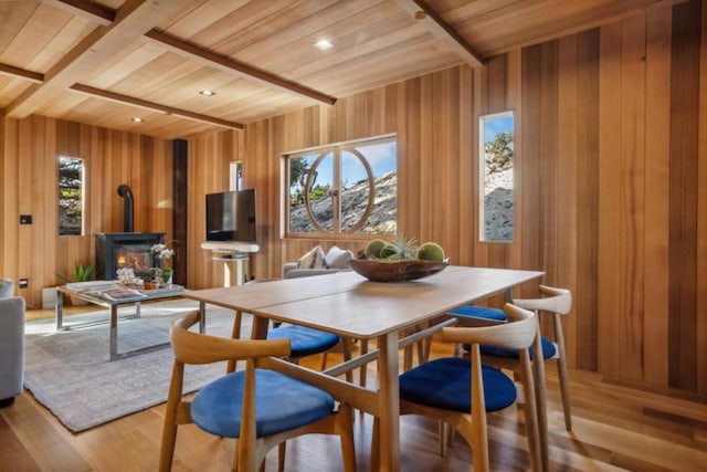 dining room with beam ceiling, light wood-type flooring, a wood stove, and wooden ceiling