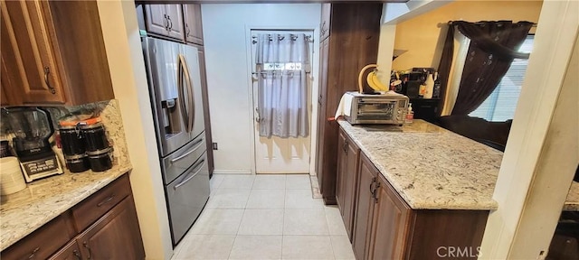 kitchen featuring light tile patterned floors, stainless steel fridge, and light stone countertops