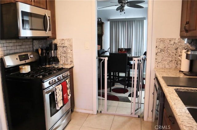 kitchen featuring light tile patterned floors, ceiling fan, stainless steel appliances, tasteful backsplash, and light stone counters