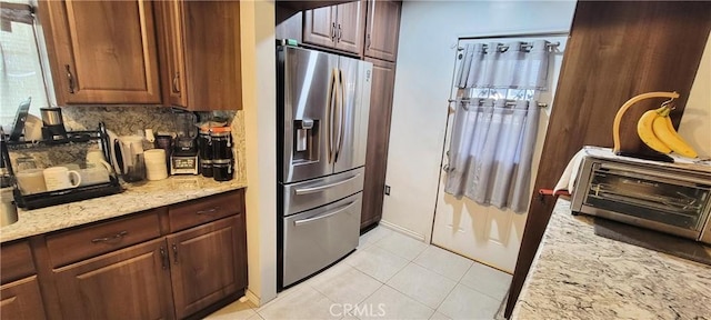 kitchen with stainless steel fridge with ice dispenser, light tile patterned floors, backsplash, and light stone counters