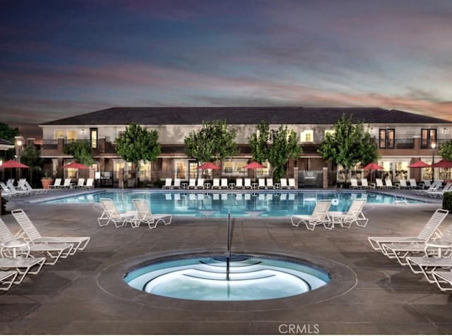 pool at dusk with a hot tub and a patio