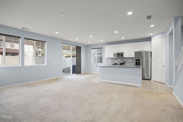 kitchen featuring white cabinets, stainless steel appliances, a center island with sink, and light colored carpet