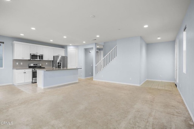 kitchen with white cabinets, an island with sink, light colored carpet, and appliances with stainless steel finishes