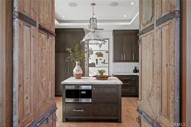 kitchen with a raised ceiling, dark brown cabinets, stainless steel oven, and light hardwood / wood-style flooring