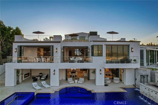 back house at dusk featuring a patio area, pool water feature, and a pool with hot tub