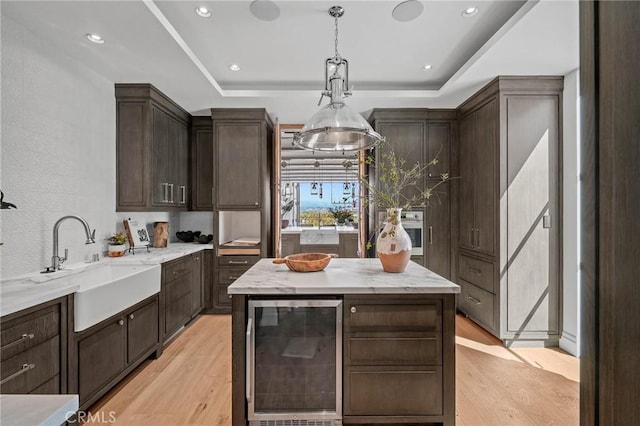 kitchen featuring a raised ceiling, light hardwood / wood-style floors, wine cooler, and sink