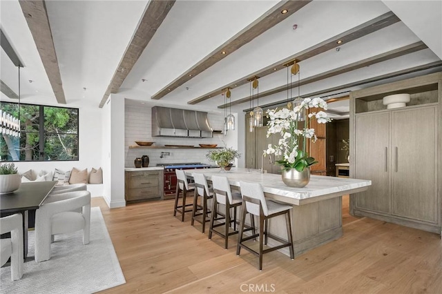 kitchen with beamed ceiling, wall chimney exhaust hood, a spacious island, and hanging light fixtures