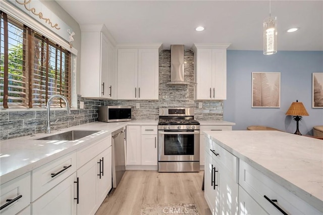 kitchen with white cabinets, wall chimney range hood, sink, and appliances with stainless steel finishes