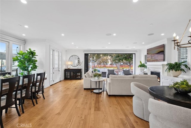 living room featuring a chandelier, light wood-type flooring, plenty of natural light, and crown molding