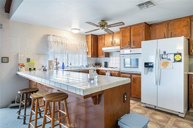 kitchen with decorative backsplash, a breakfast bar, white appliances, ceiling fan, and tile countertops