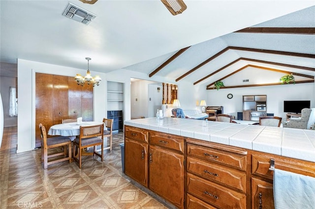 kitchen featuring lofted ceiling with beams, decorative light fixtures, an inviting chandelier, light parquet flooring, and tile counters