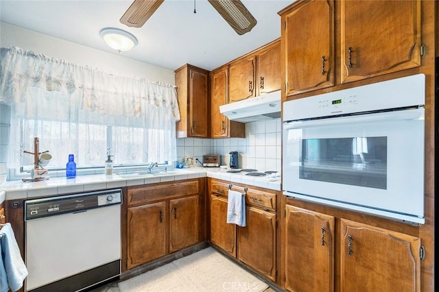 kitchen with decorative backsplash, white appliances, ceiling fan, sink, and tile counters