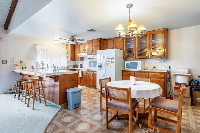 kitchen featuring tasteful backsplash, a kitchen breakfast bar, decorative light fixtures, white appliances, and ceiling fan with notable chandelier