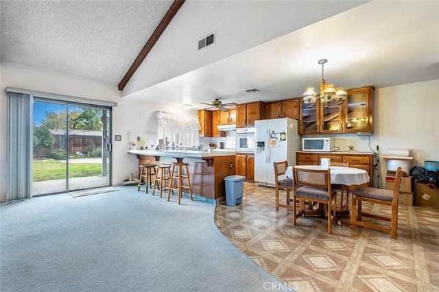 kitchen with pendant lighting, white appliances, ceiling fan with notable chandelier, vaulted ceiling, and kitchen peninsula